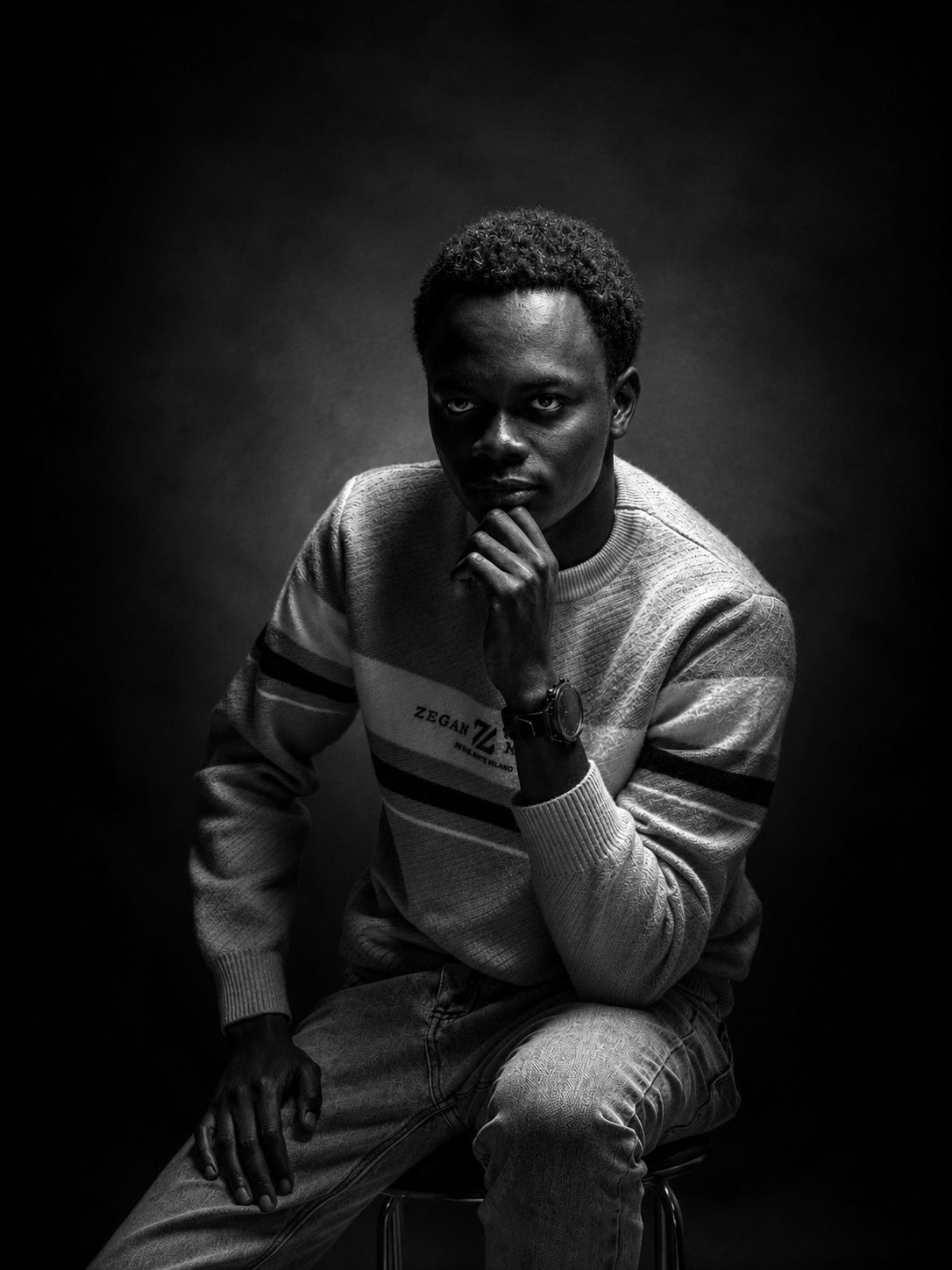 Black-and-white studio portrait of Ian Odhiambo, seated, hand on chin